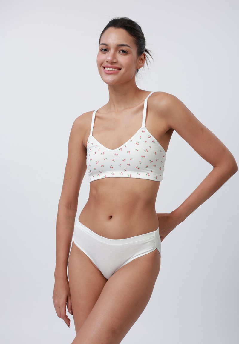 Vit bralette med liten blommig tryck och justerbara axelband, tillsammans med vita ribbade höga trosor. Slät textur genom hela.
