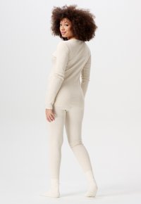Beige, langjarig bodysuit met bijpassende leggings, gemaakt van zacht materiaal. Heeft een aansluitend ontwerp en geribbelde accenten bij de manchetten en enkels.