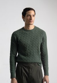 Suéter de punto trenzado verde oscuro con un escote redondo y mangas largas, que presenta patrones texturizados y puños de canalé. En general, tiene un diseño ajustado.