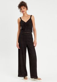 Schwarzes Spitzen-Zwei-Teiler-Outfit mit einem Cropped-Top mit verstellbaren Trägern und weit geschnittenen Hosen, beide mit einem kreisförmigen Muster.