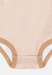 Combinaison rayée en coton doux, avec des rayures alternées de beige clair et de blanc, dotée d'ouvertures de jambes et de détails de couture en tan contrastants.