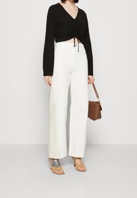 Schwarzes gekürztes Top mit Raffungen, hoch taillierte weiße weite Jeans, beige Absatzsandalen und eine kleine braune Schultertasche.
