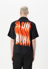 Zwarte T-shirt met korte mouwen met een grote, vurig oranje "SLOW BURN" graphic op de achterkant. Glad stof met een relaxte pasvorm.