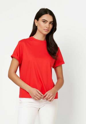 Red short-sleeve t-shirt with a round neckline and rolled cuffs, made from smooth fabric, paired with white slim-fit pants.