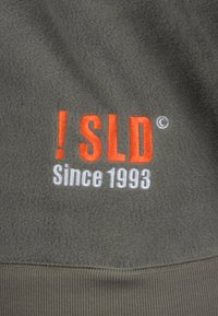 Gray fleece fabric displaying “! SLD” in orange and “Since 1993” in white, along with a ribbed waistband at the bottom.