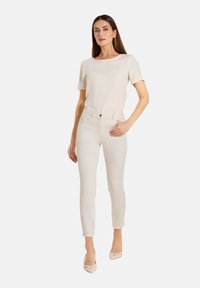 Cremfarbener Kurzarm-Top, kombiniert mit strukturierten, hellen Slim-Fit-Hosen und beigen Absätzen. Einfaches Design, durchgehend glatte Textur.