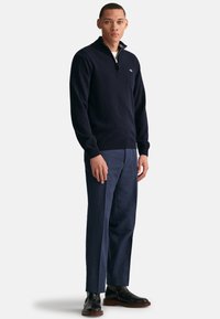 Marinekleurige trui met ritssluiting in een zachte wolmix, gecombineerd met op maat gemaakte marinekleurige broek en zwarte leren laarzen. Eenvoudig ontwerp met minimale accenten.