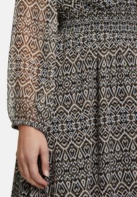 Langärmliges Kleid in einem geometrischen Muster aus Braun, Schwarz und Weiß. Verfügt über eine schmal gesmokte Taille, durchsichtige Ärmel und einen strukturierten Stoff.