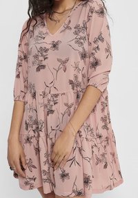 Robe rose à motif floral avec un décolleté en V, des manches trois-quarts et un ourlet à volants en couches. Fabriquée en tissu léger et texturé.