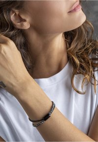 Czarna i srebrna bransoletka z dwiema splecionymi nitkami: jedna z małymi koralikami, a druga z prostokątnym czarnym akcentem.