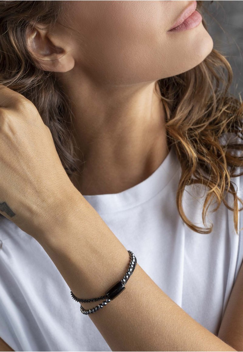 Czarna i srebrna bransoletka z dwiema splecionymi nitkami: jedna z małymi koralikami, a druga z prostokątnym czarnym akcentem.