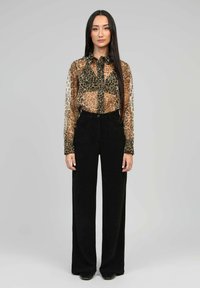 Blouse en voile imprimé léopard dans des nuances de marron et de noir, boutonnée, associée à un pantalon large noir taille haute, texture solide.