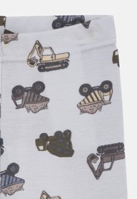 Bawełniane legginsy dla dzieci na kremowym tle z powtarzającymi się wzorami pojazdów budowlanych w kolorach brązowym, zielonym i żółtym.
