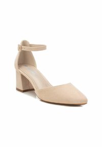 Zapatos de tacón en ante beige con punta afilada y un tacón grueso. Cuenta con una correa en el tobillo para mayor sujeción. Textura suave en toda la superficie.