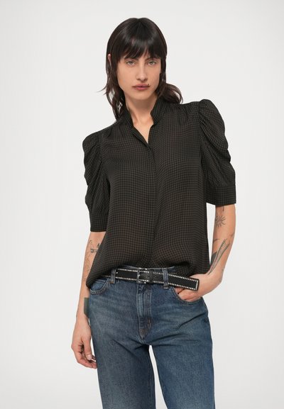 Czarna koszula w kratę z krótkimi bufkami na rękawach, kołnierzykiem i zapięciem na guziki z przodu, noszona z niebieskimi dżinsami i czarnym paskiem z ćwiekami.