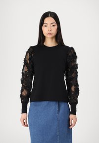 Schwarzer Sweatshirt mit transparenten Ärmeln im Blumenmuster und gerippten Bündchen, kombiniert mit einem blauen Jeansrock. Schlichtes Design und weicher Stoff.
