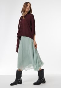 Bordeaux, oversized gebreide top gecombineerd met een vloeiende, mintgroene chiffon rok en kniehoge zwarte leren laarzen met gespaccenten.
