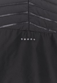 Czarny sportowy top z poziomym pikowaniem i odblaskowymi detalami. Charakterystyczny biały wzór przeszyć na dolnej części.