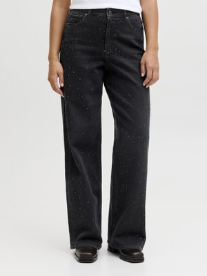 Černé džíny se širokými nohavicemi a jemnými třpytivými ozdobami, nošené s černými botami a bílým topem, zobrazené na stojící osobě.