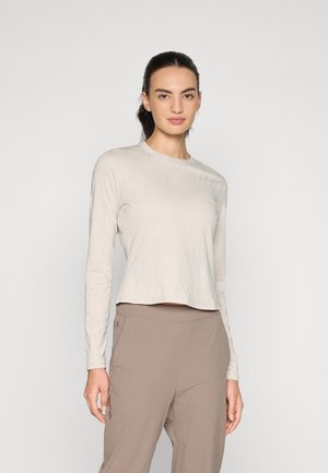 En ljus beige långärmad topp med en texturerad design, rund halsringning och kortad fåll, i kombination med ljusbruna byxor.