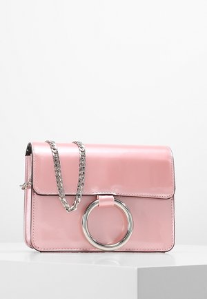 Sac à main rectangulaire rose brillant avec anneau circulaire en argent sur le rabat avant et bandoulière chaîne argent assortie reposant sur une surface blanche.