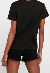 Camiseta de algodón negra con un corte relajado, escote redondo y mangas cortas, combinada con pantalones cortos de denim negro desgastados.