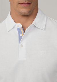 White polo shirt with a textured fabric, featuring a colored striped placket in blue and yellow, and a small logo on the chest.