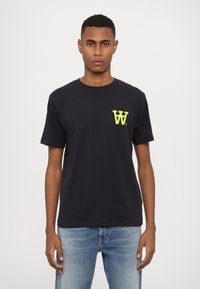 Schwarzes Baumwoll-T-Shirt mit einem gelben Buchstaben 'W' Logo auf der linken Brust, kurzen Ärmeln und einem Rundhalsausschnitt, kombiniert mit blauen Jeans.