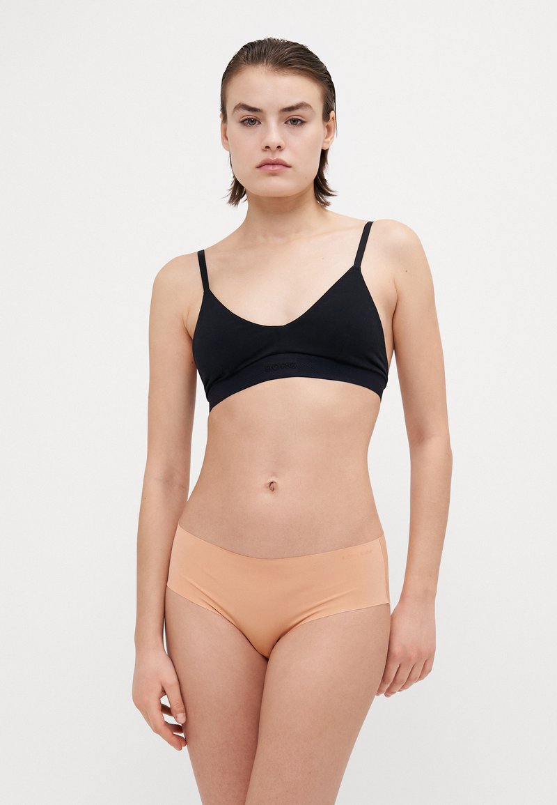 Svart trådløs bh med tynne stropper; glatt tekstur. Matchende naken sømløs hipster undertøy. Minimalistisk design, ingen synlige mønstre eller metalldeler.