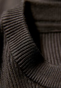 Suéter de punto canalé en tejido marrón oscuro, con un cuello alto y una textura suave, que enfatiza el diseño estructurado y el material cálido.