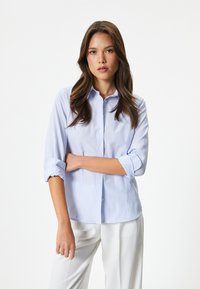 Camicia button-up a righe azzurro chiaro e bianco, con colletto, maniche arrotolate e una vestibilità rilassata. Realizzata in cotone liscio.