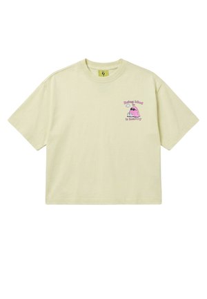 Beżowy krótki crop top z krótkim rękawem z małym różowym psem z kreskówki w okularach przeciwsłonecznych oraz tekstem "Being kind is healthy" na lewej piersi.