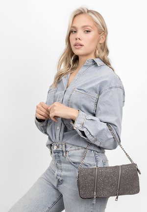 Siva crossbody torba s dva zipovana odjeljka, sjajna tekstura, lančana naramenica; nosi se uz svijetlu traper košulju i traperice.