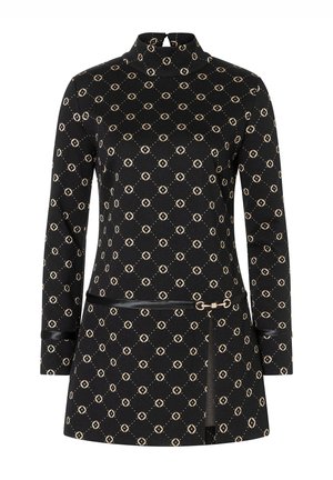 Robe noire à col montant, manches longues, avec un motif géométrique beige. Elle est dotée d'une ceinture noire fine avec une boucle dorée.
