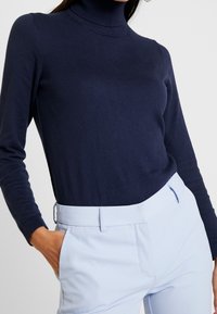 Granatowy sweter z golfem wykonany z miękkiego dzianiny, z długimi rękawami i dopasowanym krojem, zestawiony z jasnoniebieskimi spodniami o dopasowanym kroju.
