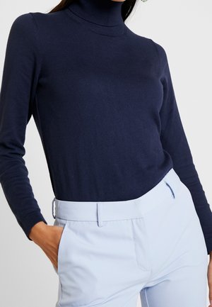 Granatowy sweter z golfem wykonany z miękkiego dzianiny, z długimi rękawami i dopasowanym krojem, zestawiony z jasnoniebieskimi spodniami o dopasowanym kroju.