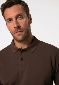 Braunes Poloshirt aus strukturiertem Stoff mit klassischem Kragen und zweiknöpfiger Knopfleiste. Das Shirt hat eine lässige Passform und kurze Ärmel.