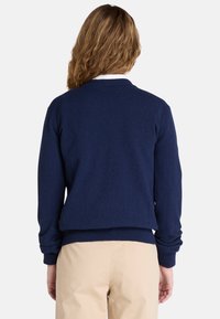 Dunkelblaues Strickoberteil mit langen Ärmeln, gerippten Bündchen und rundem Halsausschnitt. Weiche Textur mit lockerer Passform, kombiniert mit beigen Hosen.