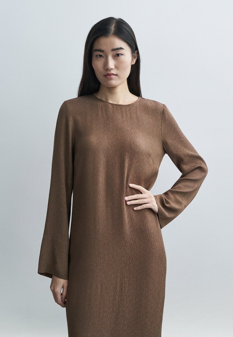 Καφέ φόρεμα μακρυμάνικο από υφασμάτινη υφή με στ�ρογγυλή λαιμόκοψη. Τα μανίκια έχουν ελαφρύ καμπύλωμα και ο σχεδιασμός είναι μινιμαλιστικός.