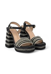 Sandalias de plataforma en blanco y negro con un diseño de tira trenzada, tacón cuadrado y correa en el tobillo. El tacón presenta rayas horizontales texturizadas.