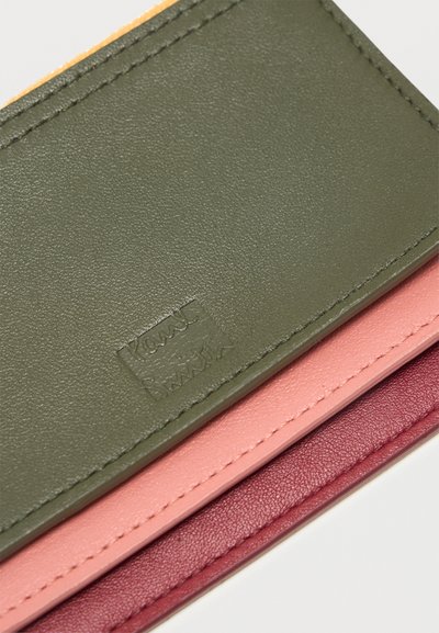 Πολύχρωμο δερμάτινο πορτοφόλι με ελαιόπρασινες, ροζ και μπορντό ενότητες, με ραμμένες άκρες και ανάγλυφο λογότυπο της μάρκας στο πράσινο μέρος.