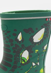 Botte de pluie en caoutchouc verte avec un motif reptilien, incluant des accents verts et noirs. Le haut possède un bord texturé avec une doublure en tissu contrastante.