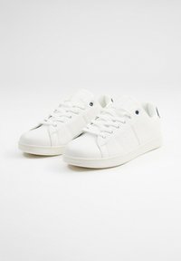 Zapatillas de deporte de imitación cuero blancas con un diseño de corte bajo, puntera redonda y suela de goma plana. Presentan un cierre de cordones y pequeños detalles en el talón.