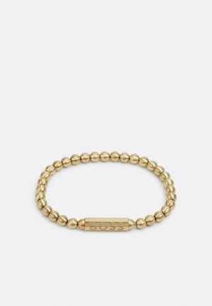 Guldtonad elastisk armband med släta, sfäriska pärlor och en platt, graverad rektangulär accent med varumärkesnamnet.