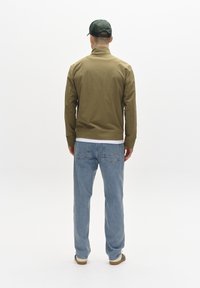 Olivegrüne, leichte Jacke mit Stehkragen, kombiniert mit hellblauen, geraden Jeans und beigen Sneakers. Schlichtes Design, keine Muster.