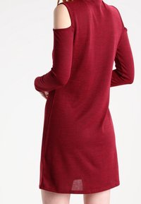 Abito borgogna a maniche lunghe con scollature sulle spalle e un tessuto morbido e testurizzato. Forma sagomata con una leggera spacco sul retro.