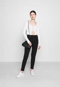 Camisola branca de mangas longas com decote arredondado e frente com cordão, combinada com jeans pretos de cintura alta e ténis brancos. Mala preta.