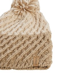Knitted beige beanie with a textured pattern, topped with a fluffy pom-pom, featuring a small leather label with "protest" printed.