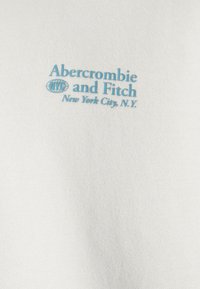 Tessuto bianco con la scritta "Abercrombie and Fitch NYC New York City, N.Y." in azzurro chiaro, progettato con una texture casual e morbida.