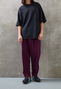 Černé bavlněné oversized tričko s malým logem, doplněné o volné tmavě fialové kalhoty a černé tenisky s barevnými akcenty.